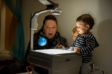 Två barn och en pedagog undersöker ljus med en overheadmaskin